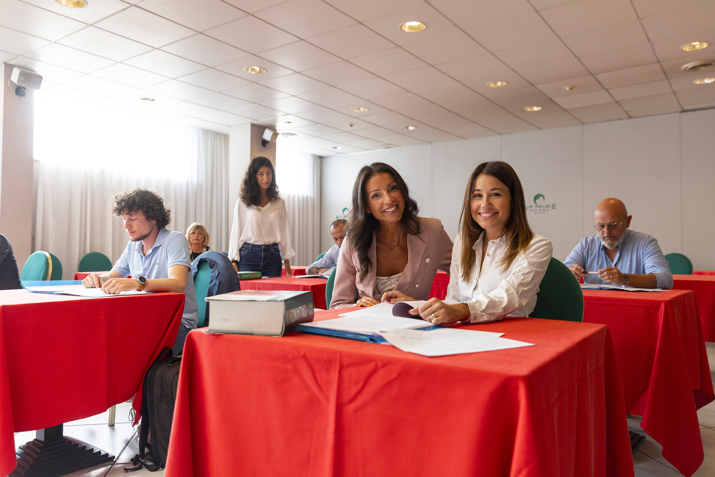 Due donne sorridono sedute a un tavolo durante una sessione di formazione aziendale con i colleghi