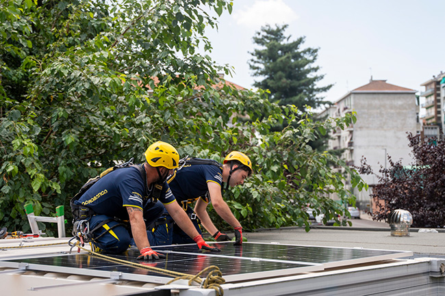 Due tecnici con casco e imbracatura installano pannelli fotovoltaici su un tetto