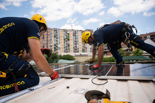 Tecnici Acrobatica con casco e dispositivi di sicurezza installano pannelli fotovoltaici su un tetto