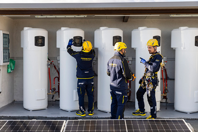 Tre tecnici Acrobatica al lavoro su scaldacqua a pompa di calore accanto ai pannelli fotovoltaici